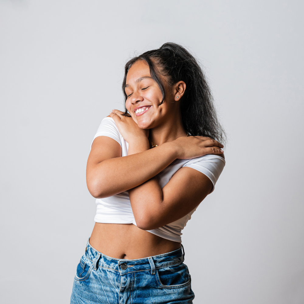 A joyous young woman hugging herself and smiling with her eyes closed, exuding self-love and confidence.