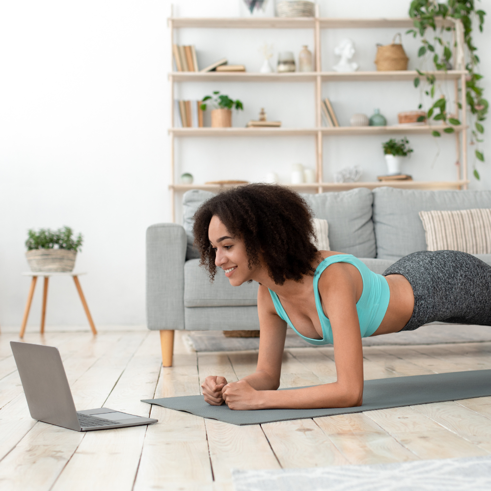 A woman engaged in a plank exercise at home, following a routine on her laptop.