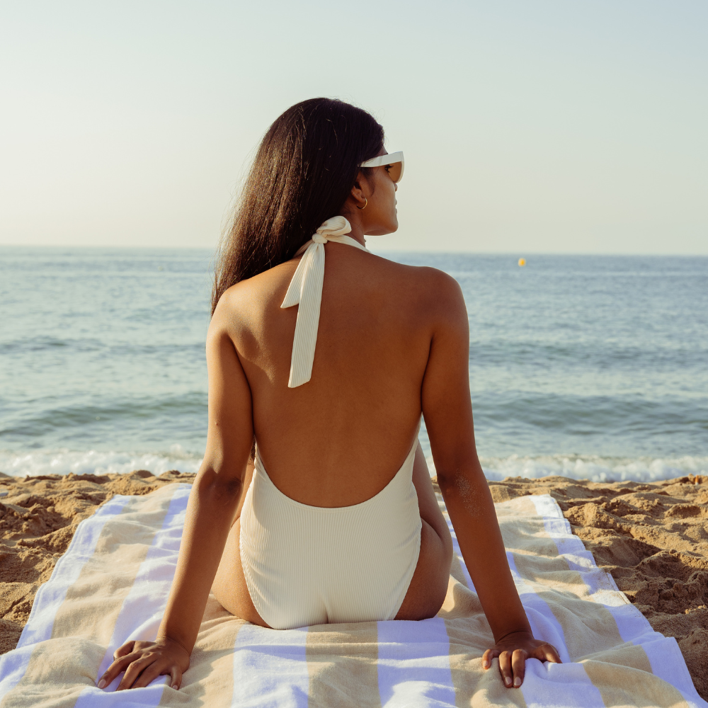 Confident beachside reflection – How to Become the Best Version of You Confident woman in white swimsuit sitting on beach towel facing the sea, embodying the best version of you spirit