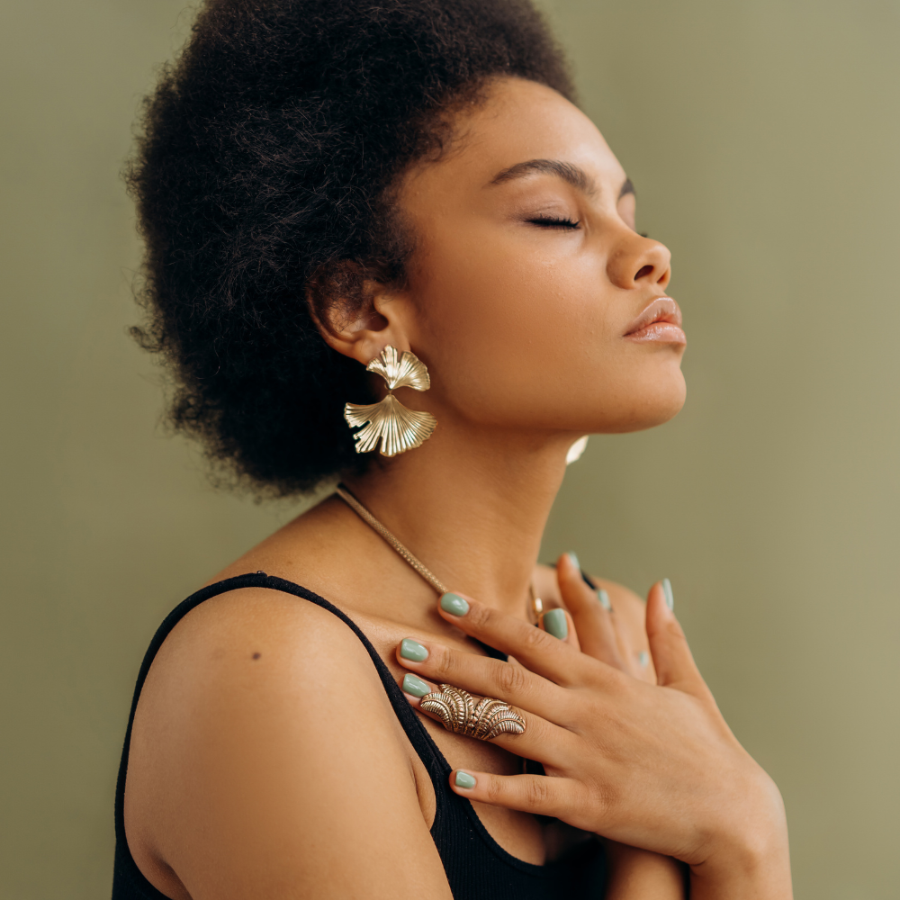 A serene woman with closed eyes, adorned with gold jewellery, practising mindfulness and self-care.