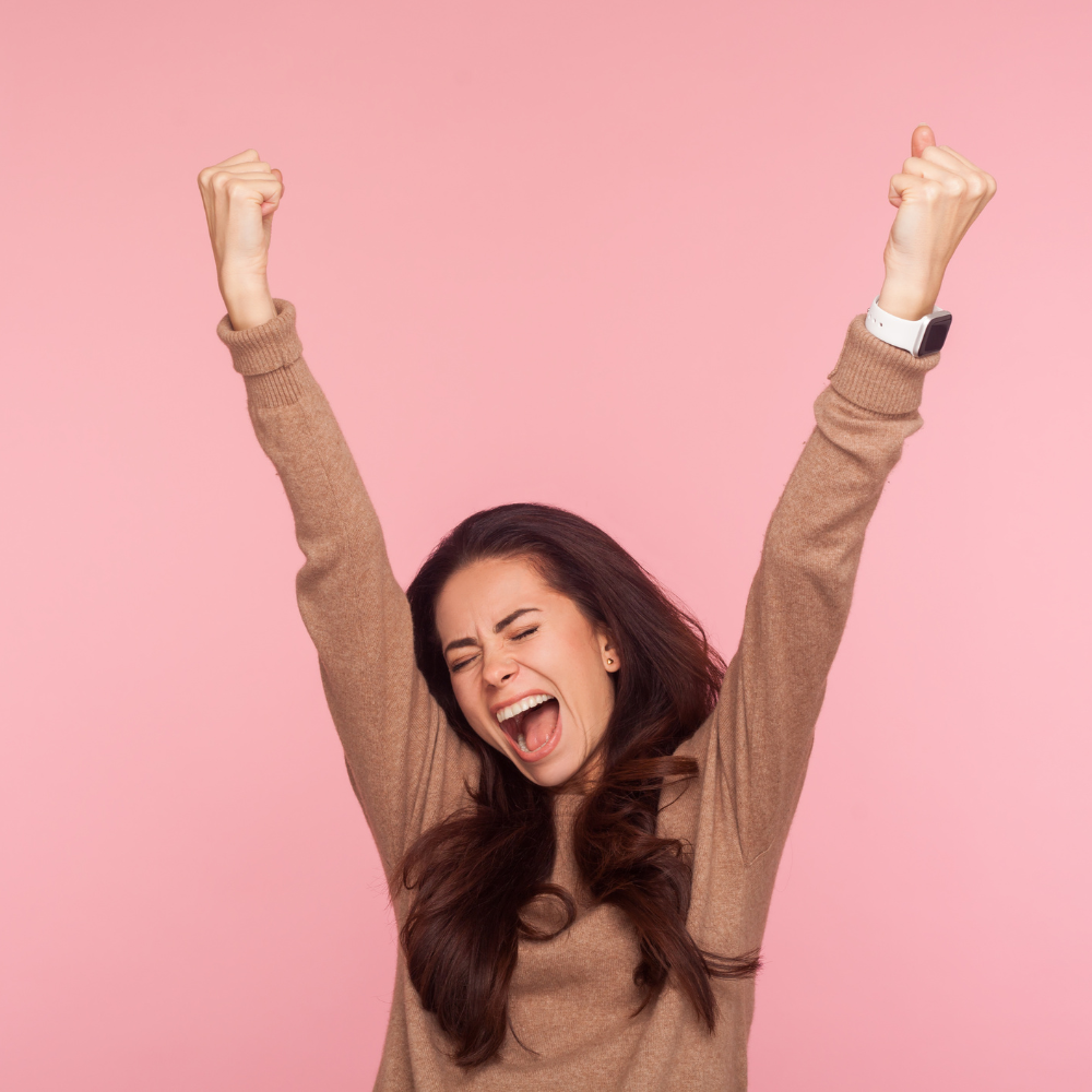 28. Triumph Over Doubt Inspiring Stories of Women Who Conquered Self-Doubt Woman celebrating with raised arms, expressing triumph and confidence against a pink background.