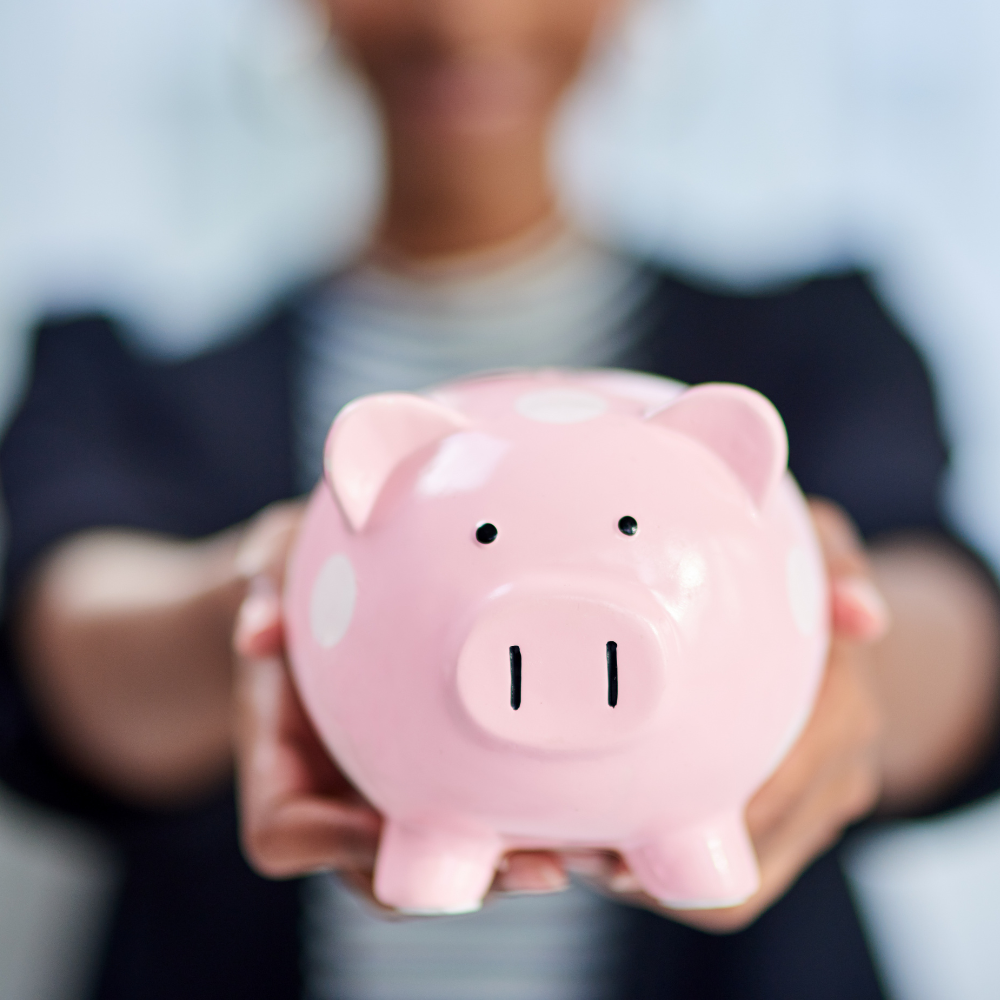 34. Achieving Financial Independence as a Woman Close-up of a woman holding a pink piggy bank with white polka dots, symbolising financial savings and independence.