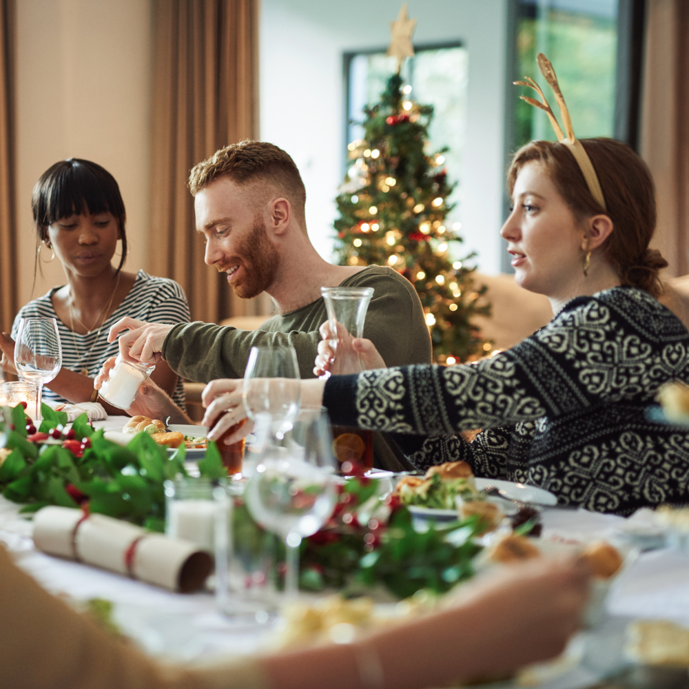 A small group of friends sharing a festive meal together in front of a Christmas tree