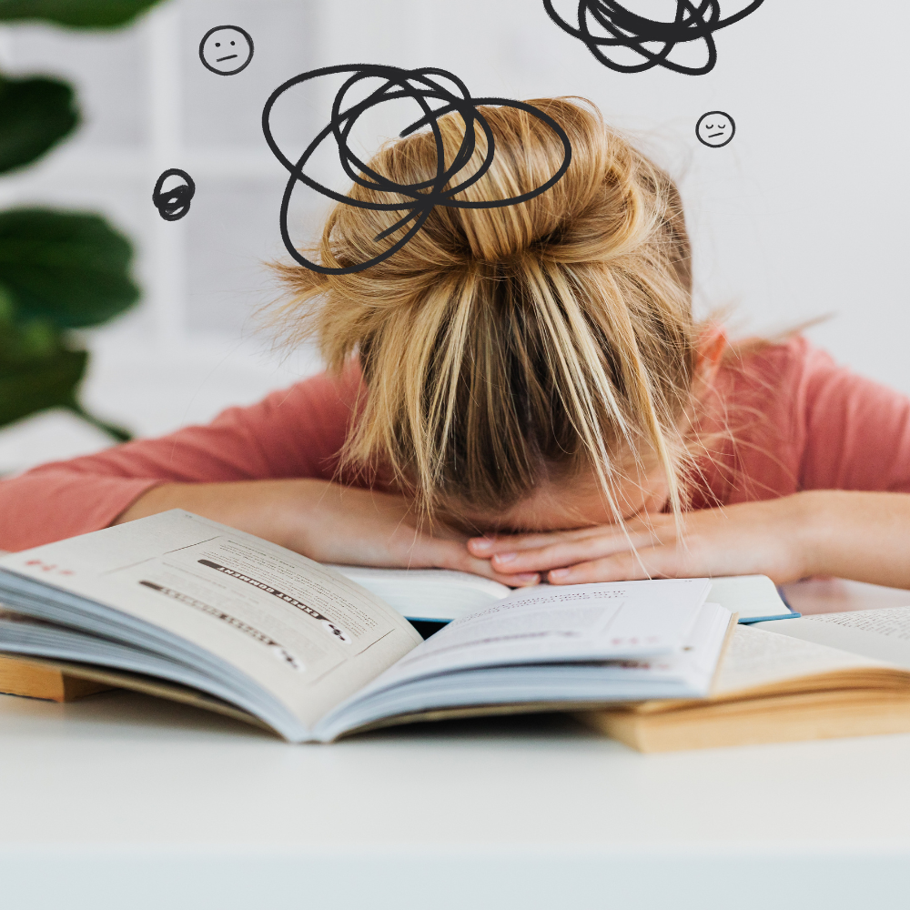 A blonde woman with a messy bun rests her head on an open book, while hand-drawn scribbles above her head represent stress and overwhelm.