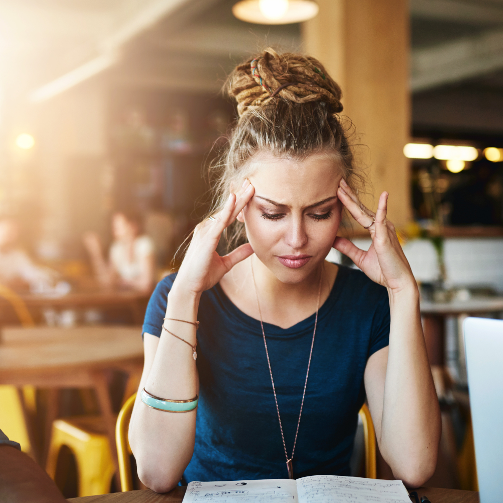 From Overthinking to Action C&C #33 Woman sitting at a café table with her hands on her temples, looking stressed while overthinking and staring at a notebook.