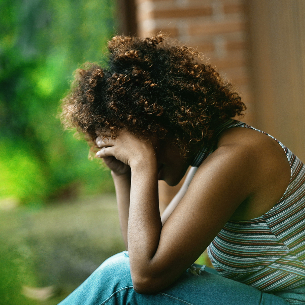 Grieving the Life You Imagined C&C #35 A Black woman sitting outdoors with her head in her hands, reflecting quietly — symbolizing grief, healing, and emotional strength.