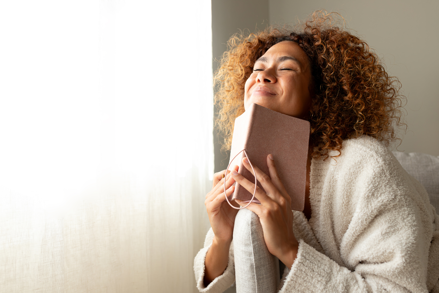 Woman smiling softly while holding a journal close to her heart, symbolizing gratitude, reflection, and manifestation practice.