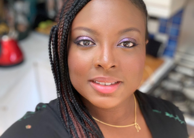 Close-up portrait of Nefe Oguntoye with braided hair and soft makeup, indoors.
