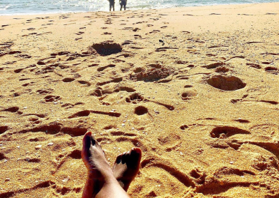 View from sandy beach looking toward the sea with two people standing near the shoreline.